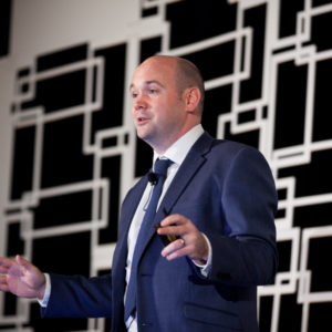 A man wearing a suit speaking at FINEOS Global Summit in 2017