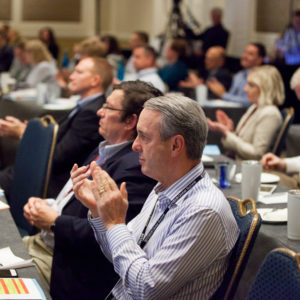 Man with striped shirt clapping at FINEOS Global Summit in 2017
