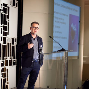 A man wearing glasses and a black jacket talking at the FINEOS Global Summit in 2017